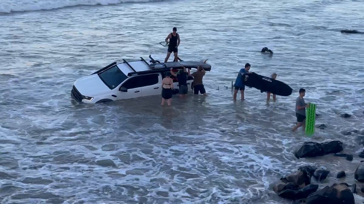 SUBMERGED: Bystanders work to free a ute from king tides off Rainbow Beach, Queensland. Picture: Bruce Howe (supplied)