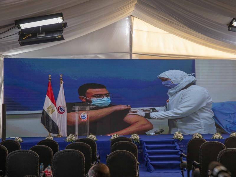 A live screen shows a doctor receiving a coronavirus vaccine as Egypt begins its rollout.